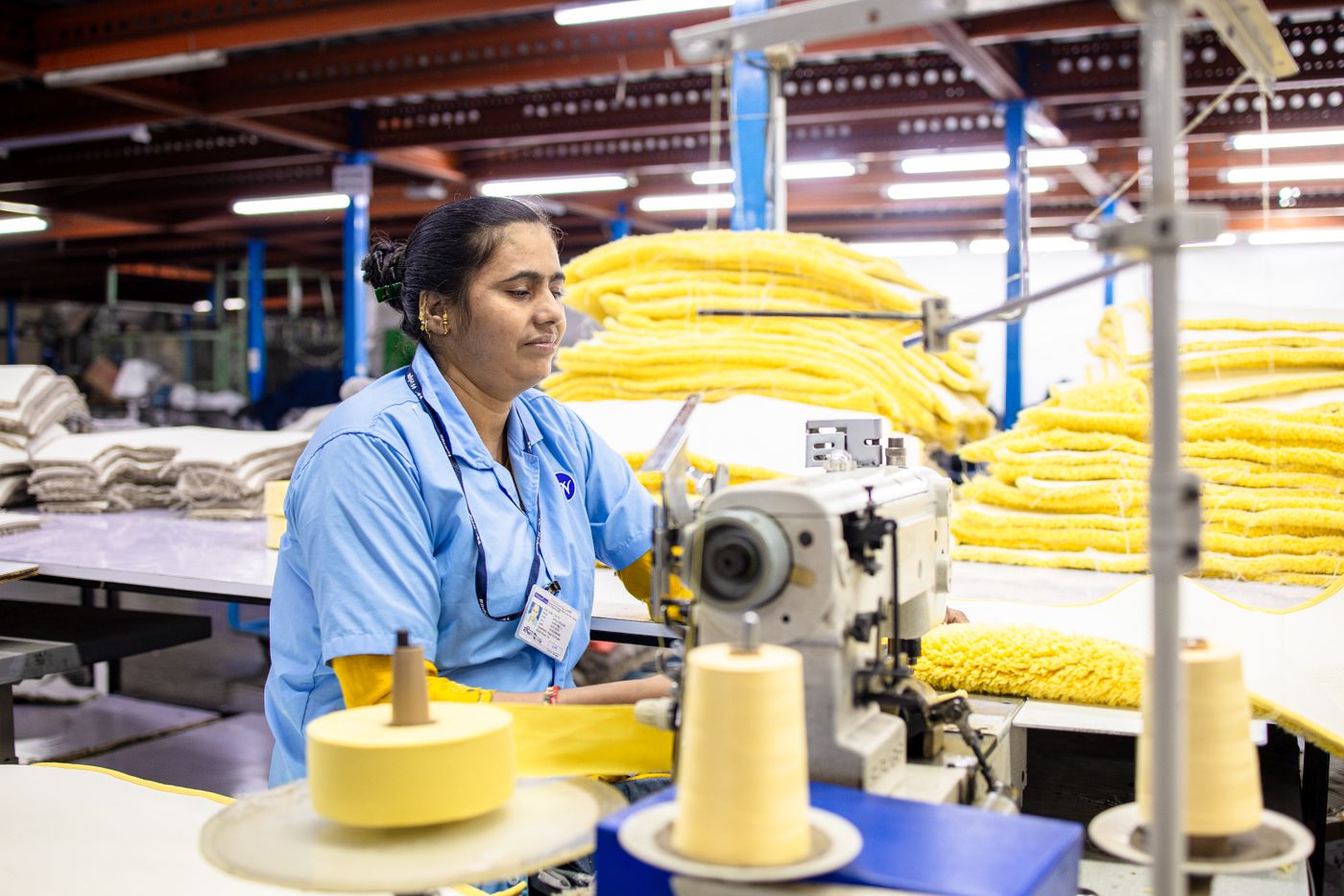 A textile worker operating an industrial sewing machine beside stacks of fabric